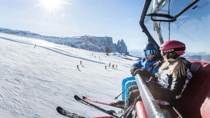 Zwei Skifahrer in einem Sessellift über schneebedeckter Piste bei klarem Himmel