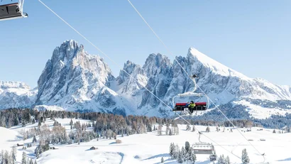 Skilift mit Fahrgästen vor schneebedeckten Bergen und blauem Himmel