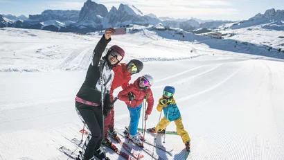 Familie macht Selfie beim Skifahren vor verschneiten Bergen